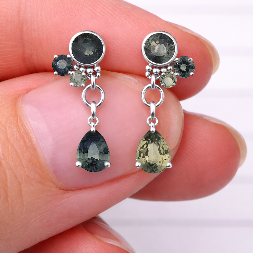 Silver earrings with green gemstones held between fingers on a white background
