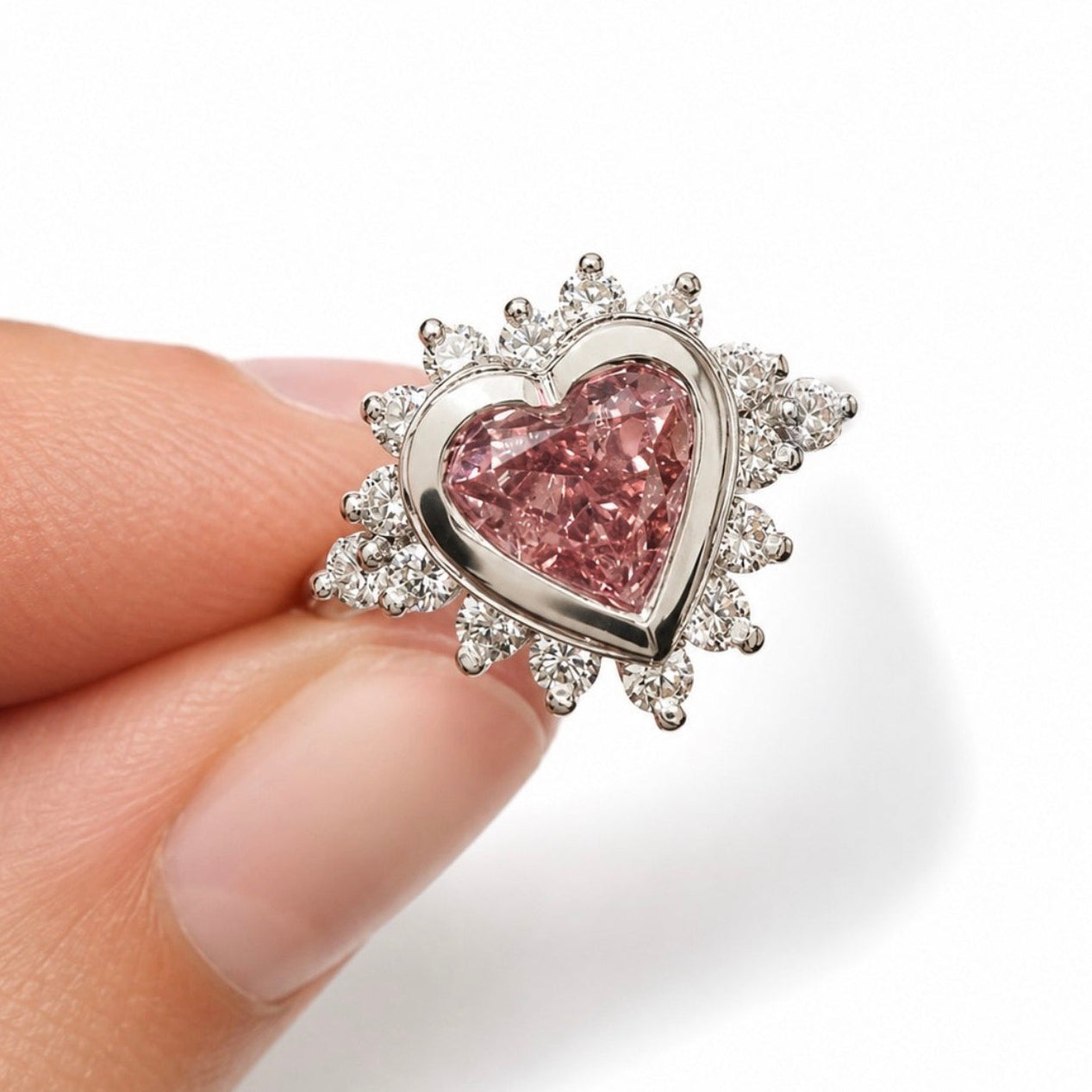 Heart-shaped pink gemstone with silver frame held by a hand against a white background