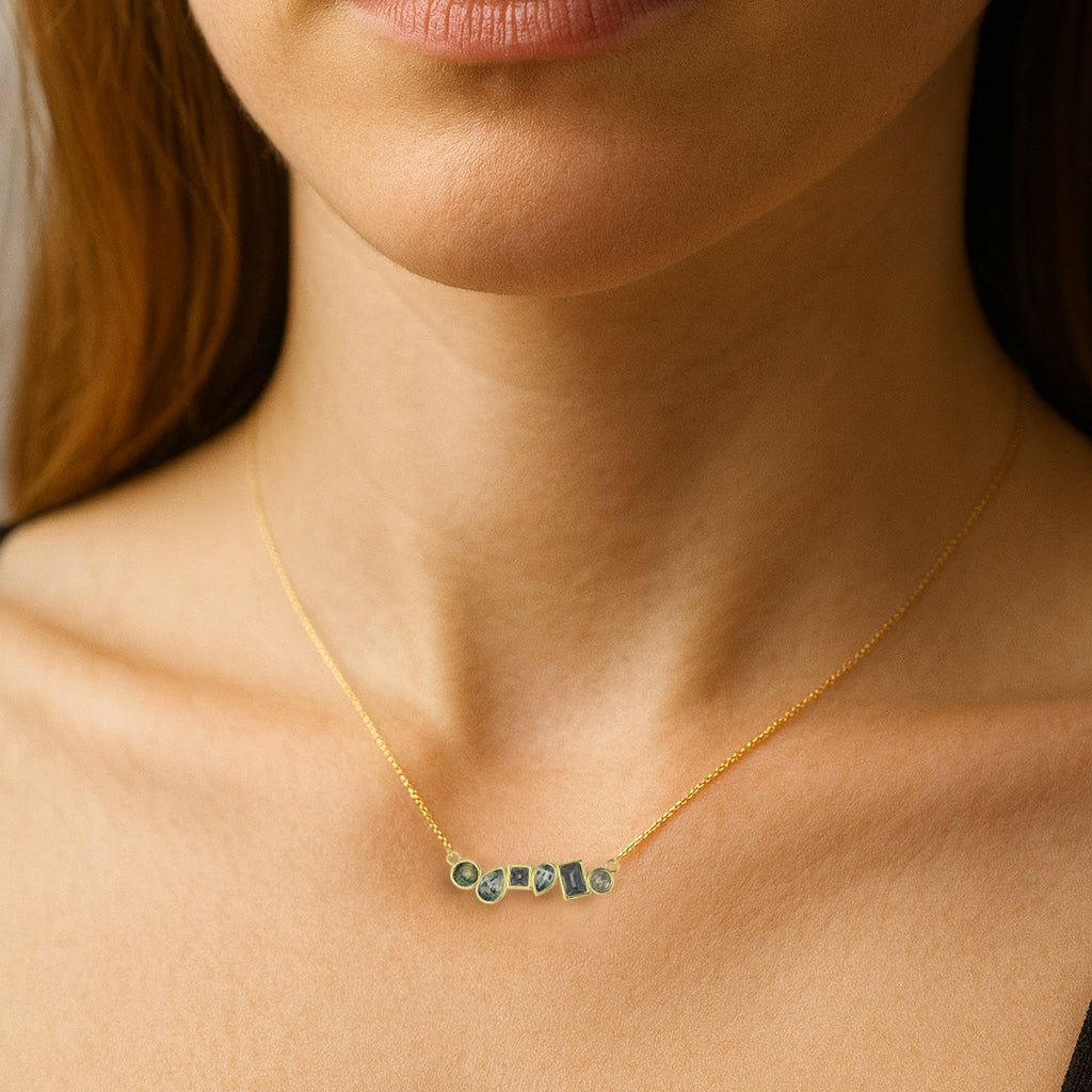 Close-up of a woman wearing a gold necklace with green gemstones.